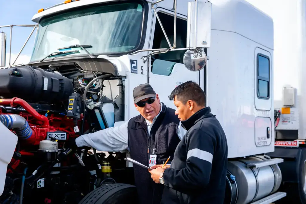 Instructor guiding student by a semi-truck engine