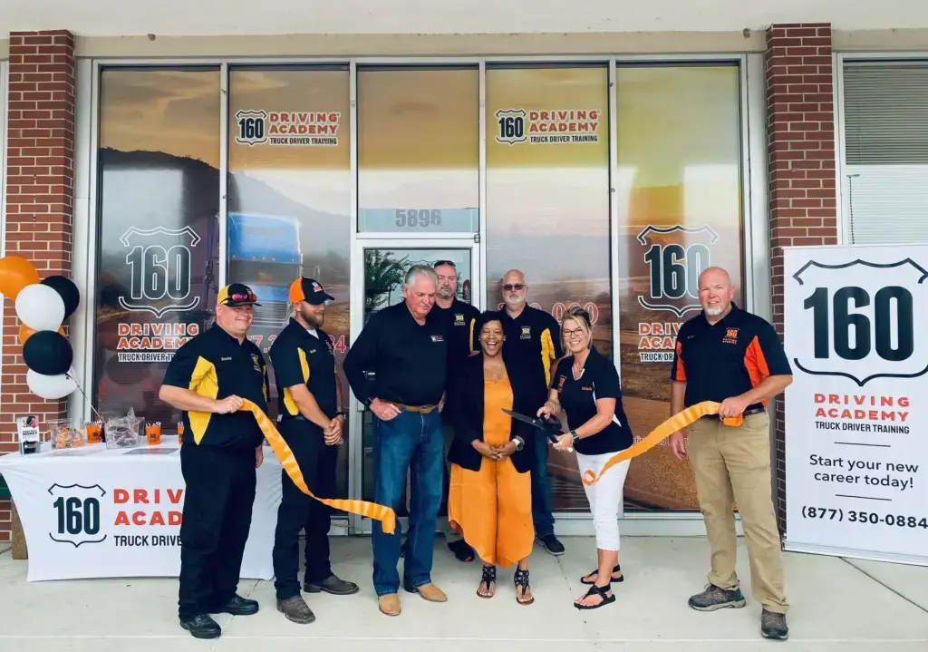 Group posing with ribbon outside 160 Driving Academy