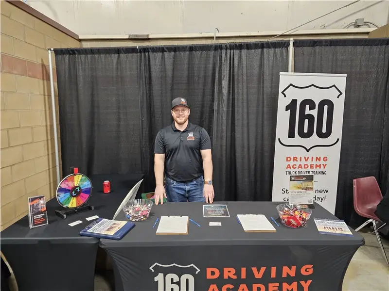 Man standing at 160 Driving Academy booth display