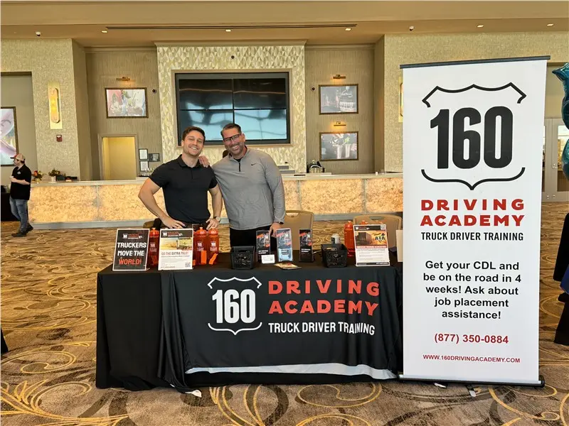 Two men smiling at a driving academy booth