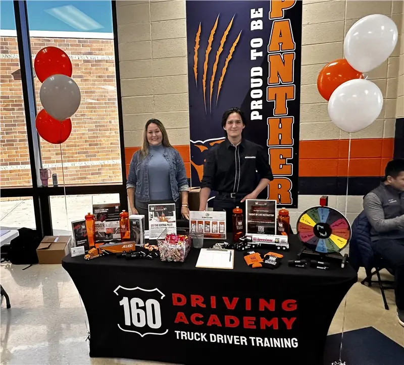 Booth showcasing 160 Driving Academy with two representatives