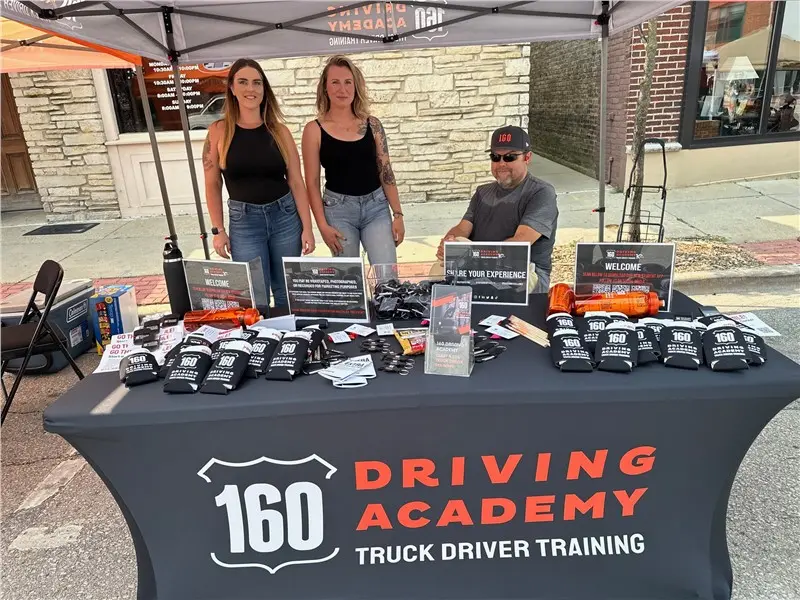 160 Driving Academy event booth with three people