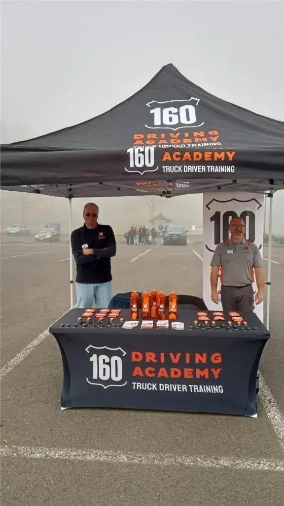 Men standing by 160 Driving Academy booth
