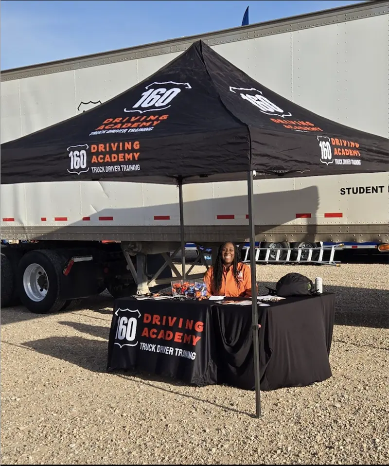 160 Driving Academy promotional booth with a smiling representative