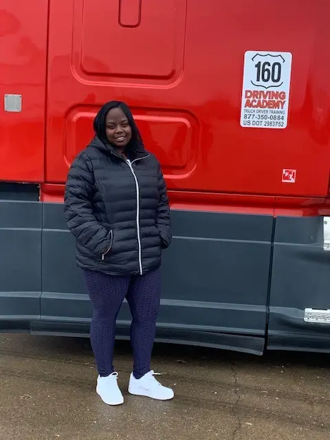 Woman smiling beside red truck at driving academy