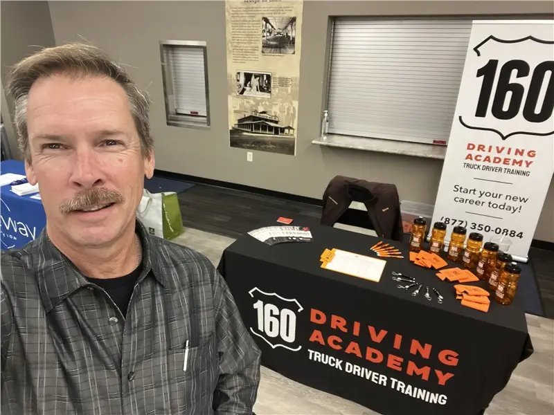 Man smiling at 160 Driving Academy booth display