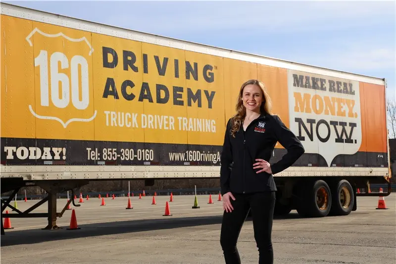 Smiling woman standing beside driving academy truck