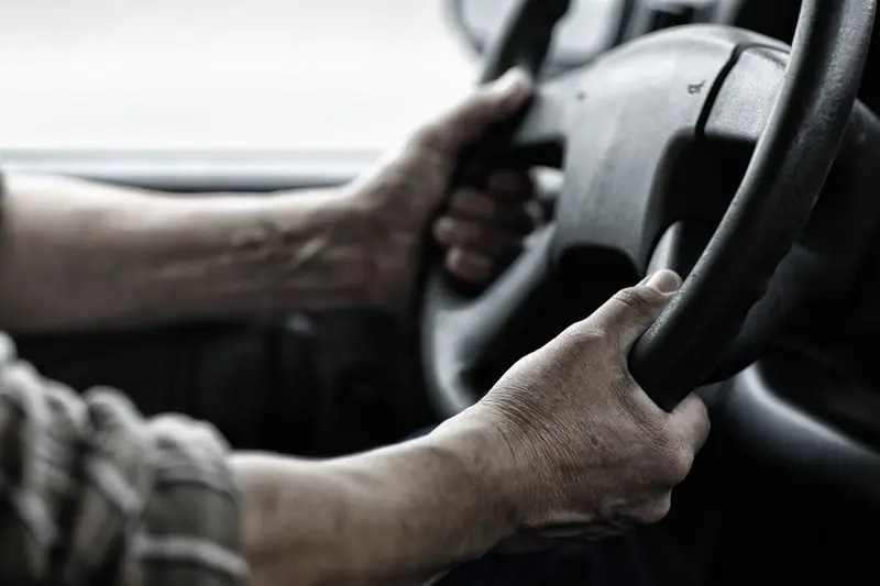 Hands gripping black steering wheel firmly inside vehicle