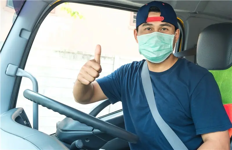 Driver wearing mask giving thumbs up in vehicle