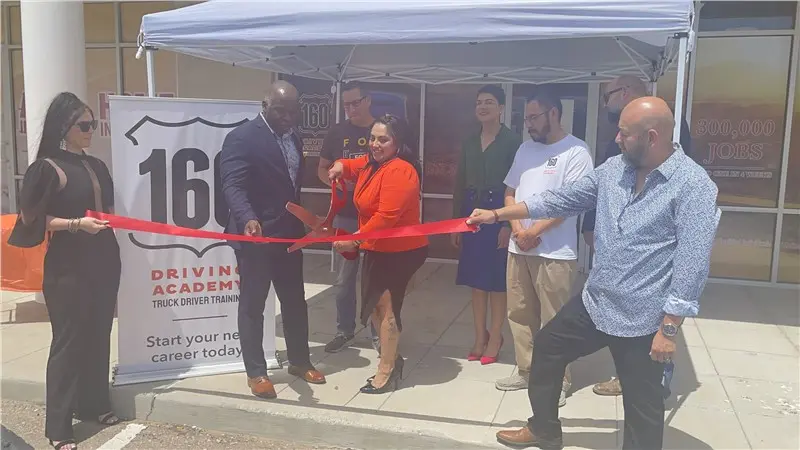 Group cutting red ribbon at outdoor ceremony