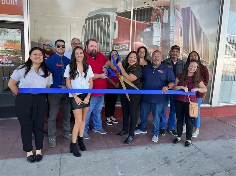People celebrate ribbon cutting with large blue ribbon