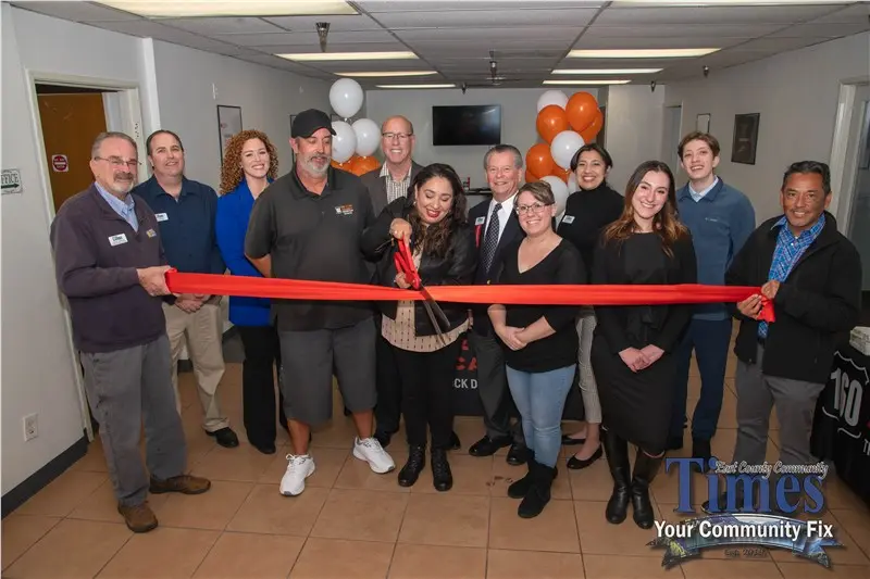 Group cutting ribbon at ceremony with large scissors