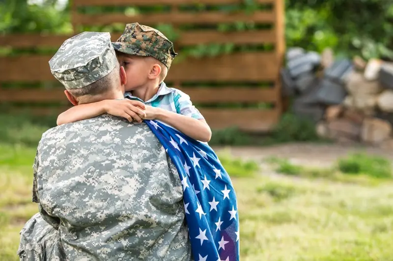Child hugging soldier, draped in American flag