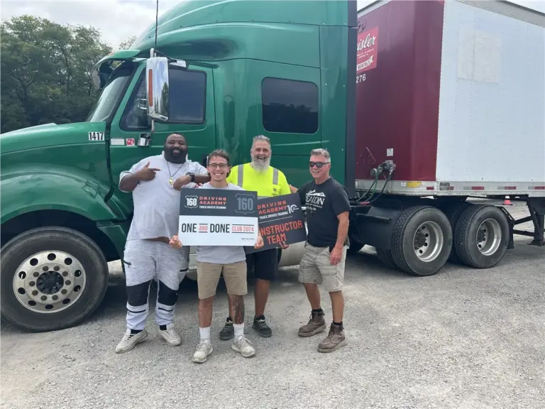 Graduated students holding certificates by green truck