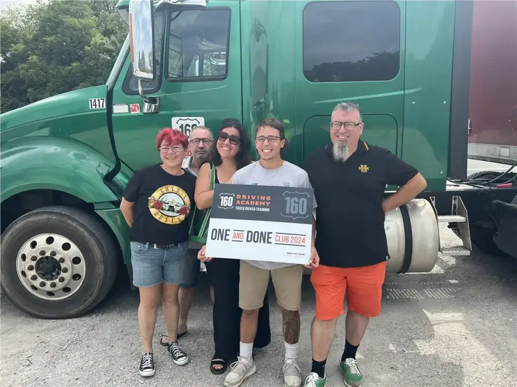 Graduates holding certificate beside semi-truck, smiling together