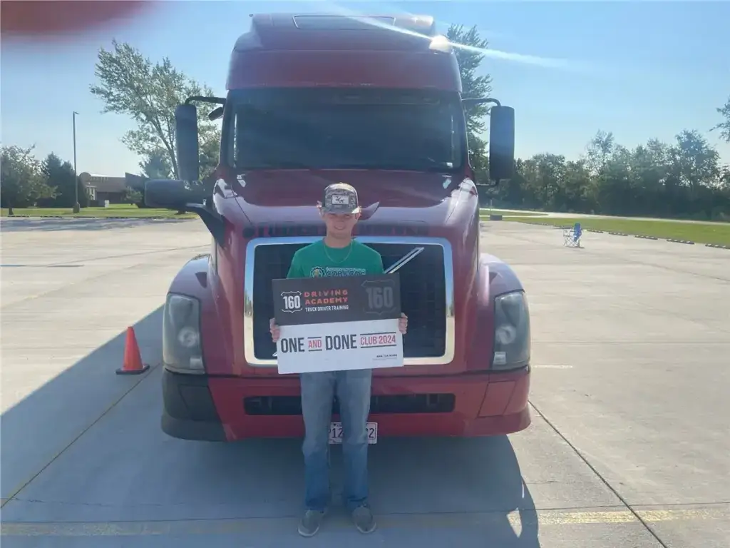 Graduate holding certificate in front of red truck